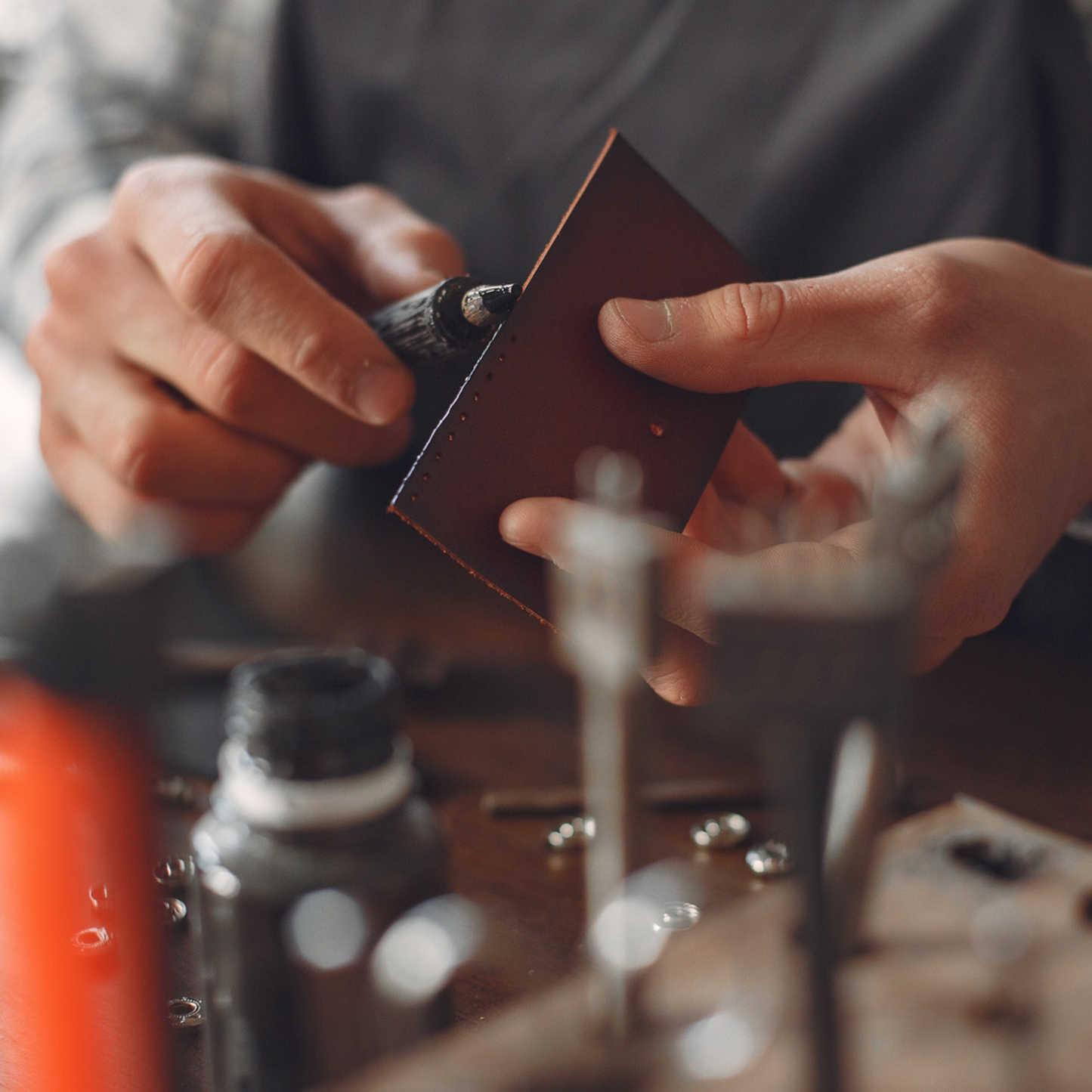 Artisan hand-varnishing the edges of a handcrafted leather accessory, highlighting precision and traditional leathercraft techniques.